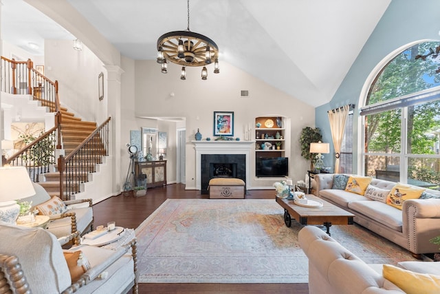living room with a notable chandelier, high vaulted ceiling, built in shelves, stairs, and wood finished floors