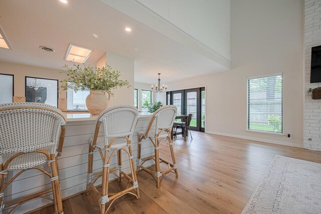 dining room featuring baseboards, light wood finished floors, a chandelier, a high ceiling, and recessed lighting