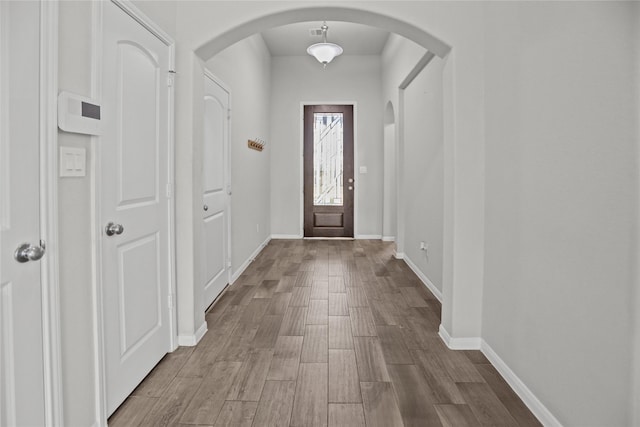 entrance foyer with baseboards, arched walkways, and wood finished floors