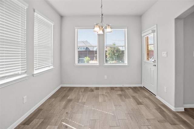 unfurnished dining area featuring baseboards, a notable chandelier, a healthy amount of sunlight, and wood finished floors