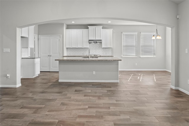 kitchen with under cabinet range hood, arched walkways, white cabinets, and backsplash