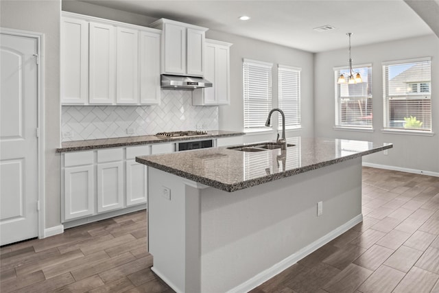 kitchen with tasteful backsplash, a sink, white cabinets, dark stone counters, and under cabinet range hood