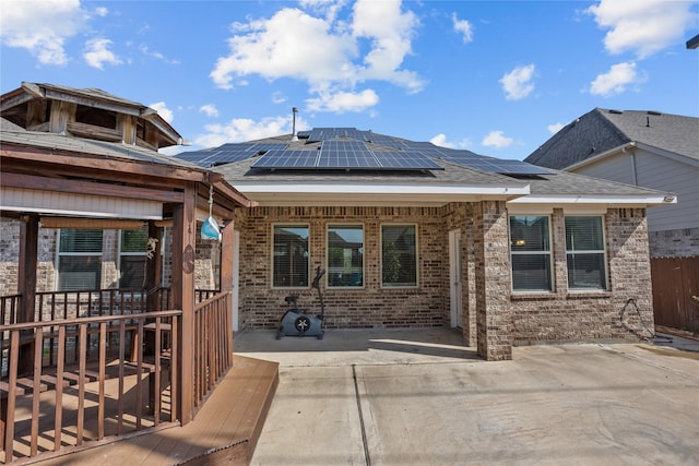 rear view of property with fence, roof with shingles, brick siding, solar panels, and a patio area