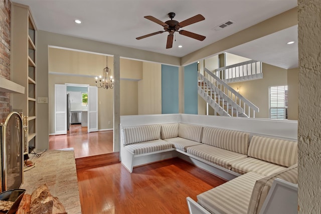 living area featuring a fireplace, ceiling fan with notable chandelier, stairs, wood finished floors, and visible vents