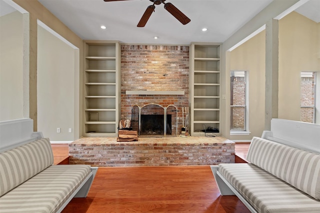 living room with baseboards, ceiling fan, a brick fireplace, and built in shelves