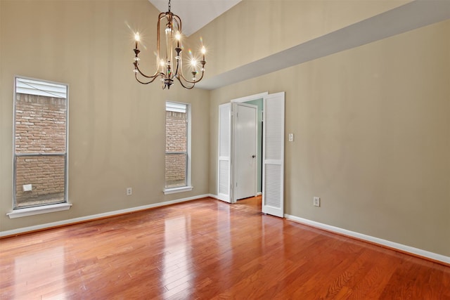 empty room featuring baseboards, wood finished floors, a chandelier, and high vaulted ceiling