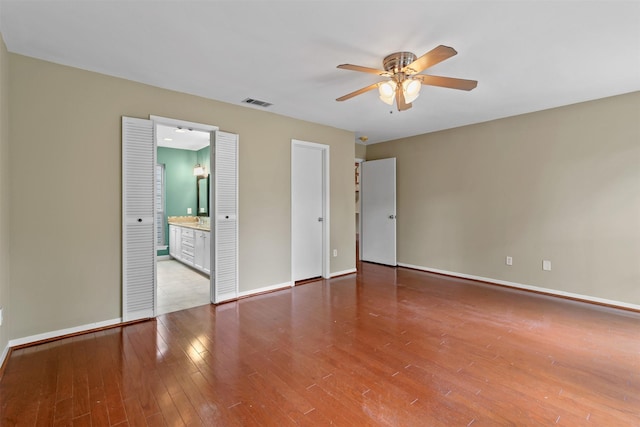 unfurnished bedroom with a ceiling fan, baseboards, wood finished floors, ensuite bathroom, and visible vents