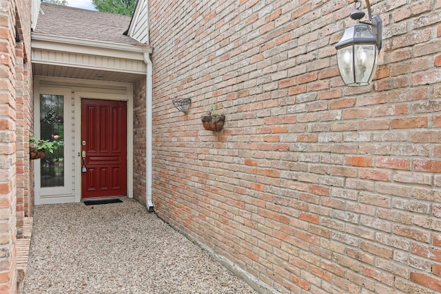 property entrance featuring a shingled roof and brick siding
