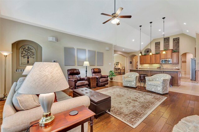living room featuring light wood-style floors, arched walkways, ceiling fan, and high vaulted ceiling