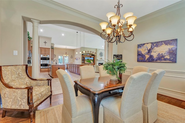 dining area with arched walkways, ornamental molding, light wood finished floors, and a chandelier