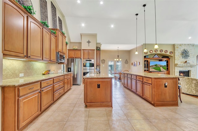 kitchen with decorative backsplash, light stone countertops, open floor plan, a large island with sink, and stainless steel appliances