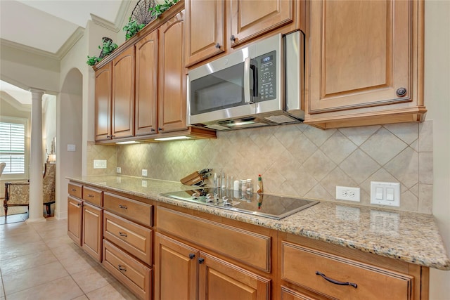 kitchen with ornamental molding, decorative columns, light stone countertops, black electric stovetop, and stainless steel microwave