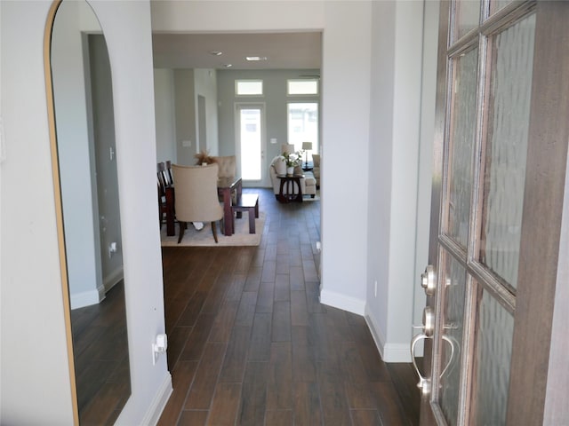 corridor with dark wood-style flooring, baseboards, and arched walkways