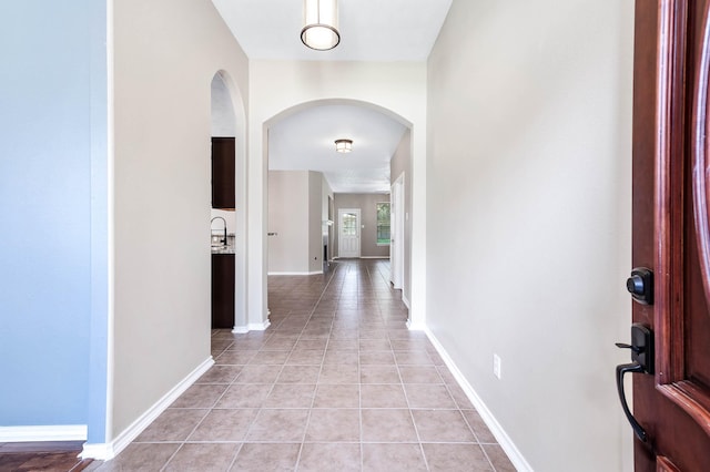 corridor with arched walkways, light tile patterned flooring, and baseboards