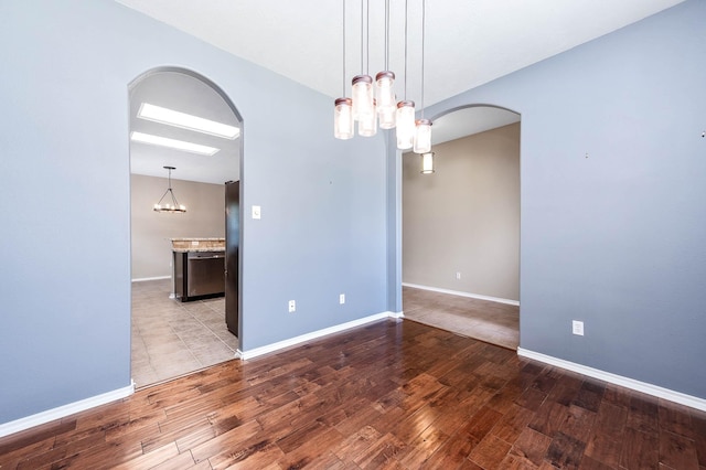 spare room with arched walkways, a chandelier, wood finished floors, and baseboards