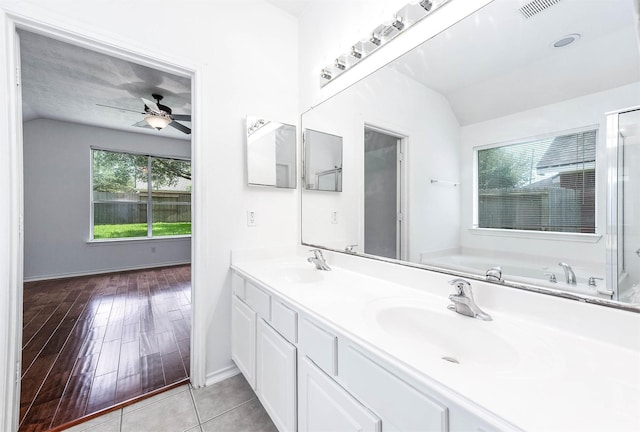 full bath with vaulted ceiling, ceiling fan, a bath, double vanity, and baseboards