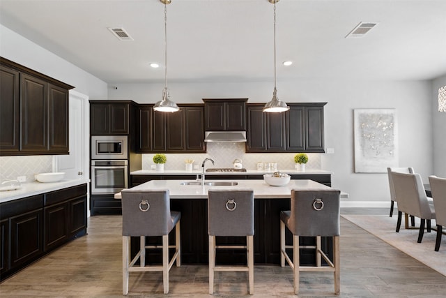 kitchen with appliances with stainless steel finishes, under cabinet range hood, a center island with sink, and visible vents