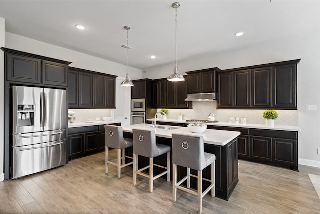 kitchen featuring appliances with stainless steel finishes, a sink, a breakfast bar area, tasteful backsplash, and under cabinet range hood