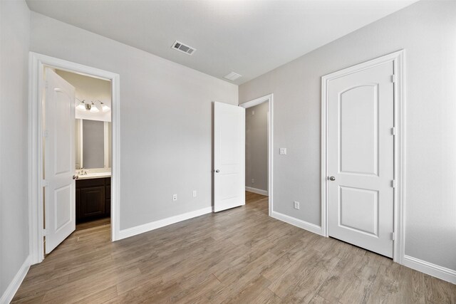 unfurnished bedroom with visible vents, baseboards, ensuite bathroom, and light wood-type flooring
