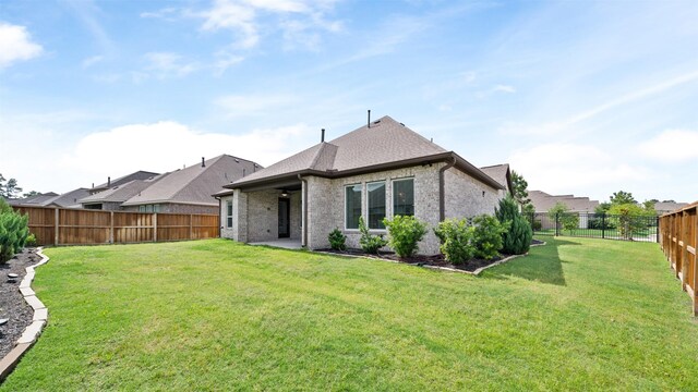 rear view of house with a yard, brick siding, a fenced backyard, and roof with shingles