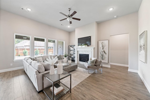 living room with visible vents, wood finished floors, baseboards, a high end fireplace, and a ceiling fan