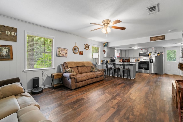 living area featuring a ceiling fan, visible vents, and dark wood-style floors