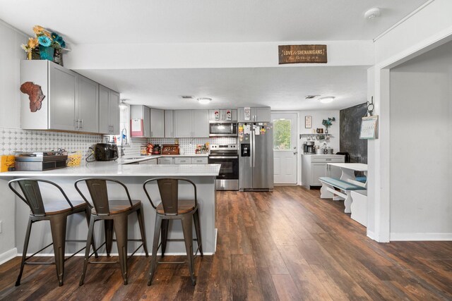 kitchen with a peninsula, dark wood-style floors, tasteful backsplash, appliances with stainless steel finishes, and gray cabinetry