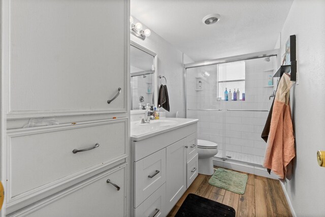 bathroom featuring vanity, wood finished floors, toilet, and a shower stall