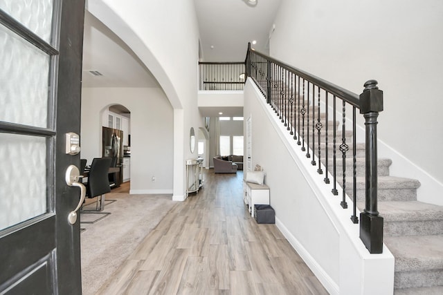 foyer entrance with visible vents, arched walkways, wood finished floors, a high ceiling, and stairs