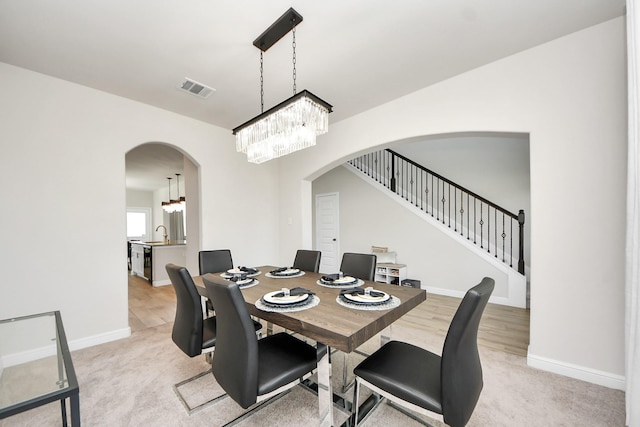 dining room featuring light colored carpet, visible vents, arched walkways, baseboards, and an inviting chandelier