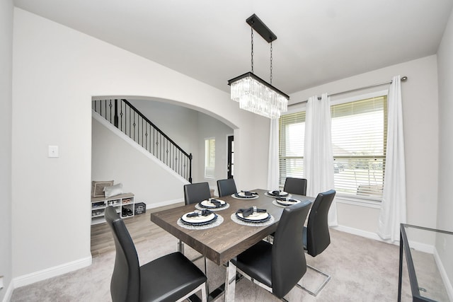dining space featuring baseboards, arched walkways, a notable chandelier, and light carpet