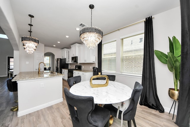 dining area with visible vents, arched walkways, light wood-style floors, and a notable chandelier