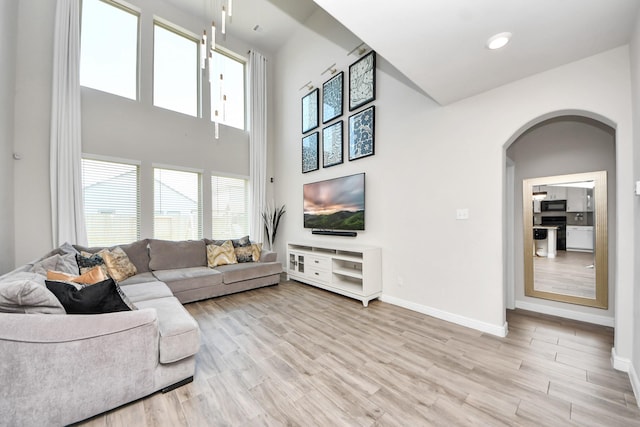 living room featuring a healthy amount of sunlight, arched walkways, baseboards, and light wood-type flooring