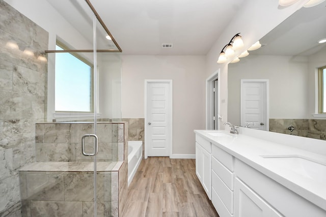 full bathroom with double vanity, a garden tub, a shower stall, wood finished floors, and a sink
