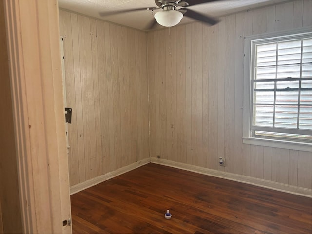 empty room featuring baseboards, wooden walls, ceiling fan, and dark wood-style floors