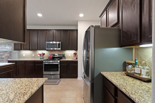 kitchen with dark brown cabinetry, light stone countertops, tasteful backsplash, light tile patterned floors, and stainless steel appliances