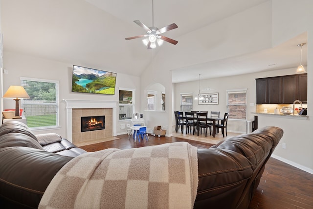 living room with baseboards, ceiling fan, dark wood-style floors, high vaulted ceiling, and a tiled fireplace