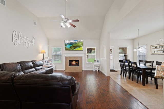 living area with hardwood / wood-style flooring, visible vents, a tiled fireplace, and ceiling fan with notable chandelier