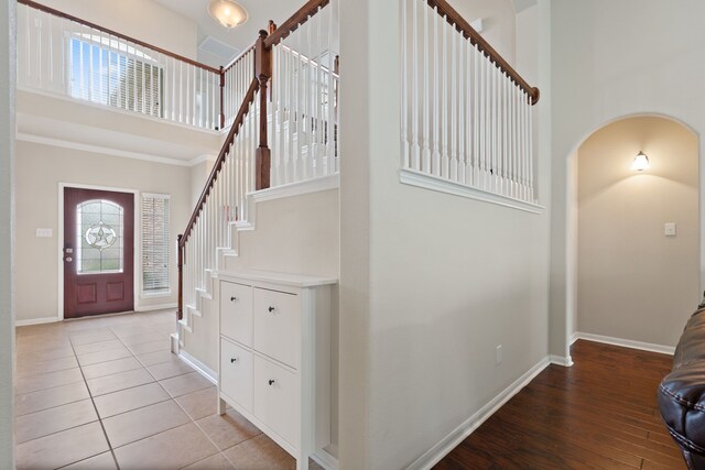 foyer featuring crown molding, baseboards, a high ceiling, arched walkways, and light wood finished floors