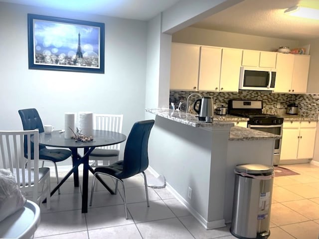 13415 Naples Bridge Rd, Sugar Land, TX 77498 - kitchen featuring light stone counters, stainless steel gas stove, a peninsula, light tile patterned floors, and backsplash