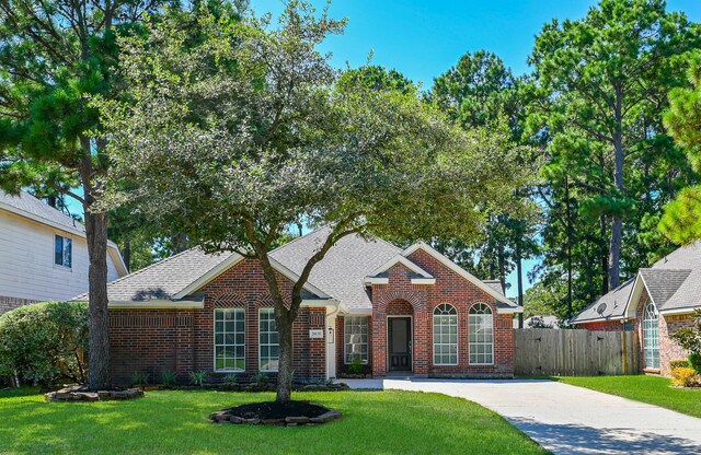 view of front of home featuring fence, a shingled roof, a front yard, and brick siding