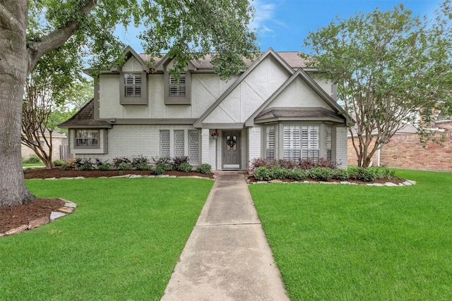 tudor home featuring a shingled roof, stucco siding, a front yard, and brick siding