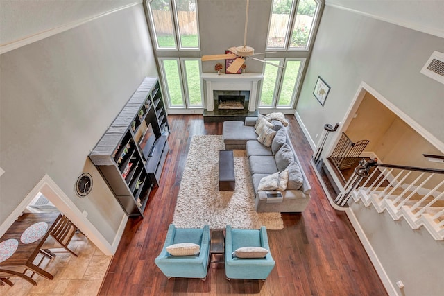 living area featuring visible vents, a towering ceiling, hardwood / wood-style floors, baseboards, and a high end fireplace
