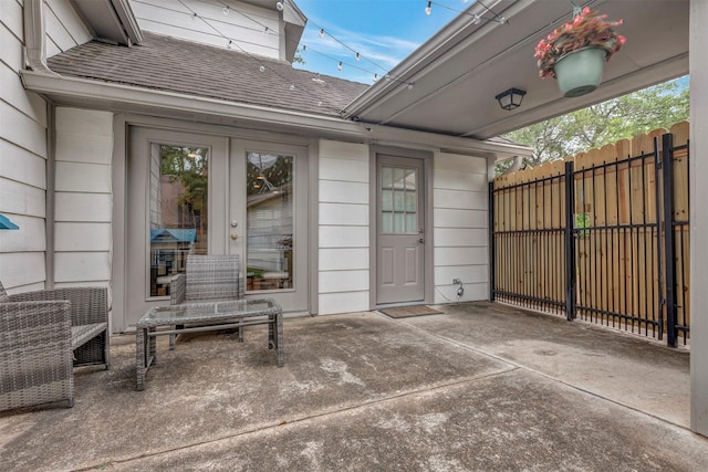 property entrance with fence, a shingled roof, and a patio area