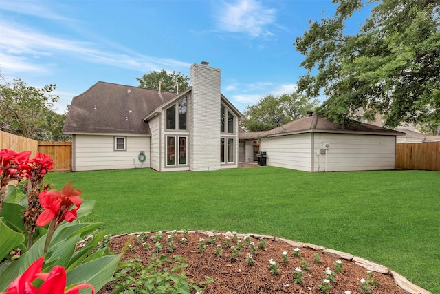 rear view of house featuring a yard, a shingled roof, a chimney, and a fenced backyard