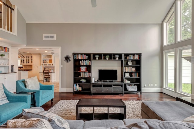 living room with visible vents, baseboards, a towering ceiling, and dark wood-style floors