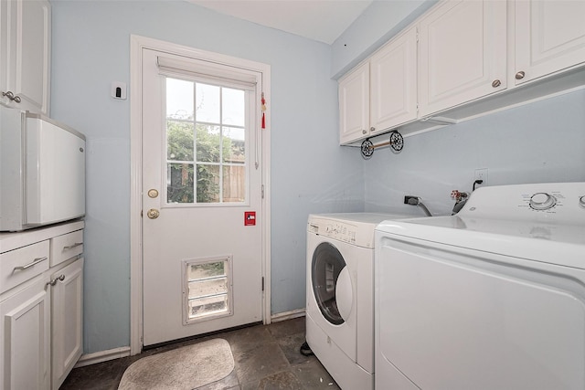 laundry area featuring baseboards, washer and clothes dryer, cabinet space, and stone finish floor