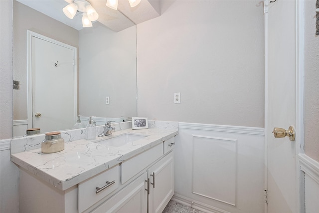 bathroom featuring vanity, a ceiling fan, wainscoting, and a decorative wall