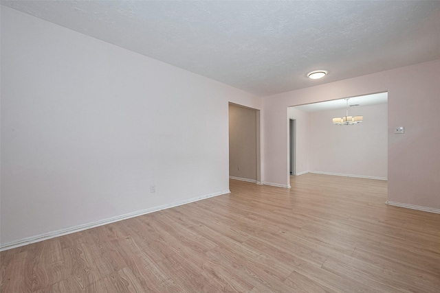 empty room with a textured ceiling, baseboards, a chandelier, and light wood finished floors