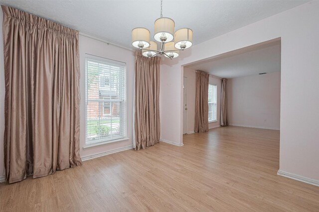 empty room with baseboards, light wood finished floors, and a notable chandelier